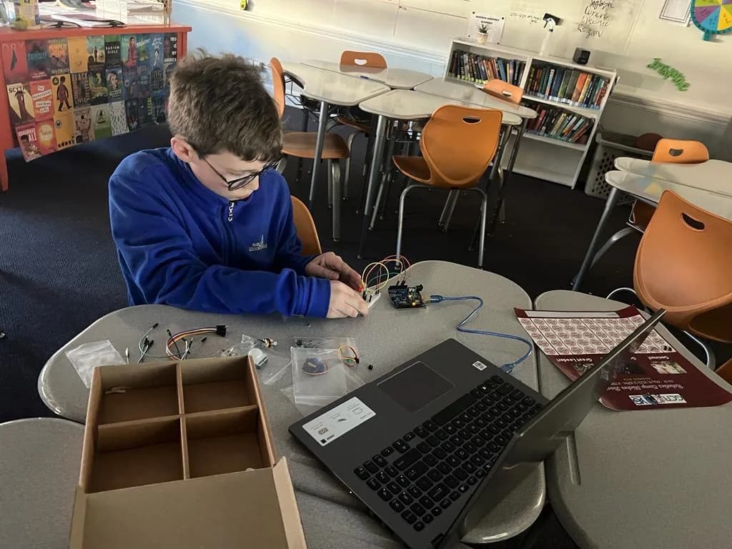 A child connecting an electronics project beside a laptop